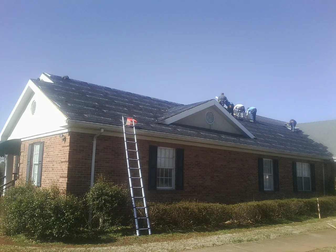 Crew tearing shingles off a brick ranch roof with a ladder set — Metal Roof Repair work by our crew in Hillsborough